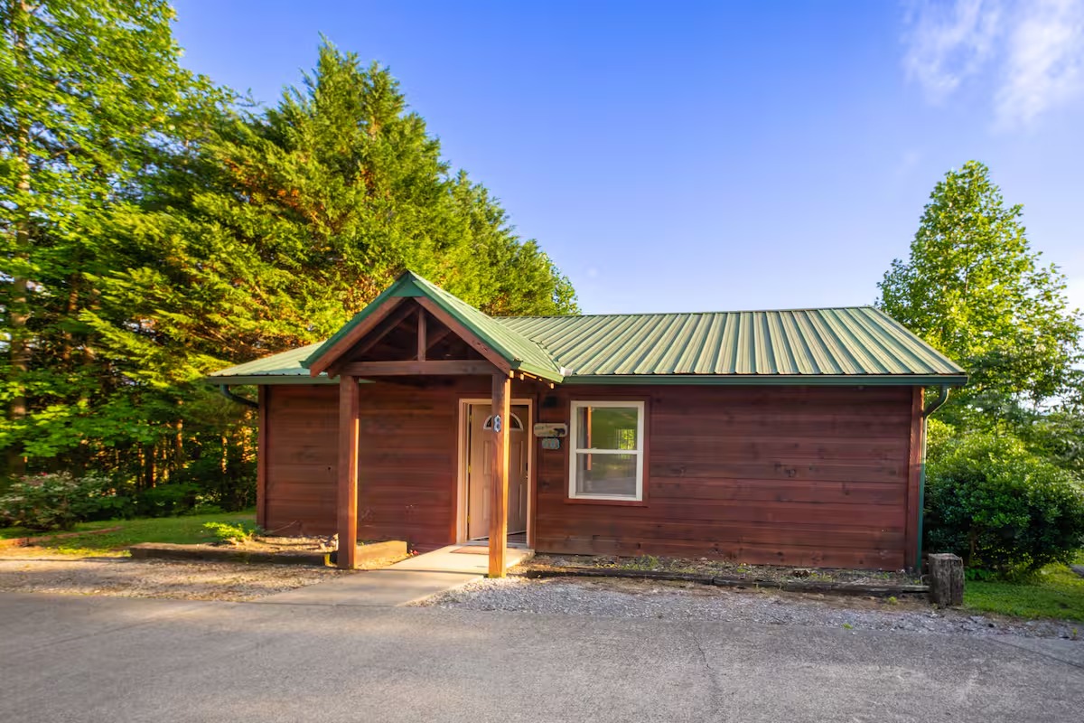 The exterior of a single-story brown wooden cabin with a green metal roof.