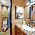 Bathroom vanity with a patterned tile countertop, a large metal-framed mirror, and a wood-paneled toilet nook.