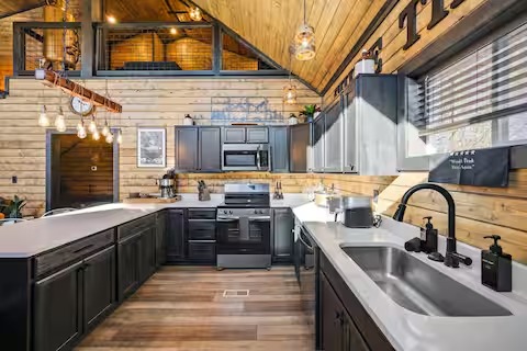 Modern U-shaped kitchen with dark cabinetry, white countertops, and stainless steel appliances under a vaulted wood ceiling.