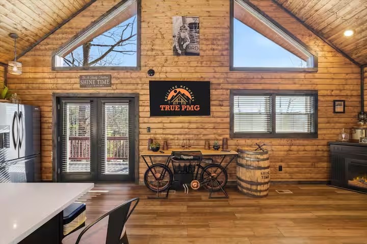 A rustic living room with wood-paneled walls, a leather sofa, a fireplace, and a unique whiskey barrel table.